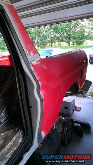 Red vehicle body panel being prepped for paint, with plastic sheeting inside the door frame