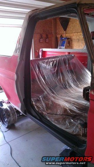 1978 Ford Bronco interior with plastic-covered seats and red exterior paint, undergoing restoration