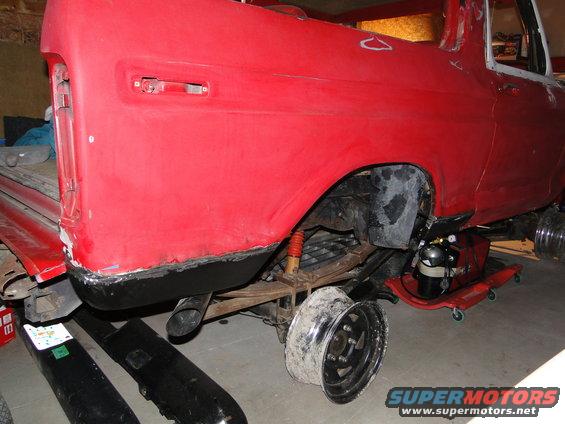 Red 1978 Ford Bronco rear quarter panel, undergoing restoration, with exposed suspension and a detached wheel