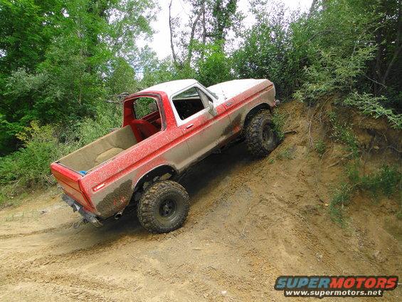 Red and white Ford pickup truck climbing a dirt hill off-road