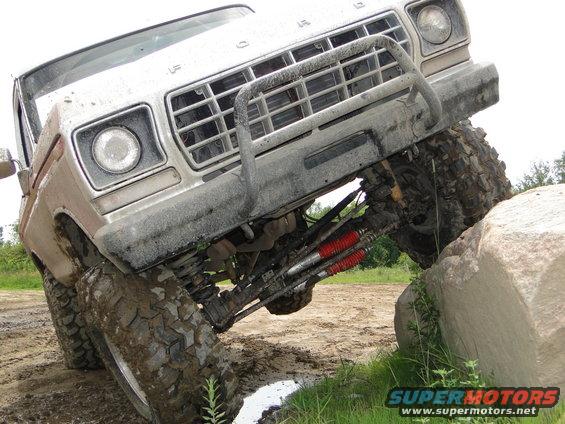 Silver Ford truck with off-road tires climbing a large rock, front grille visible