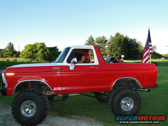 Side view of a lifted red and white 1978 Ford Bronco with an American flag in the background