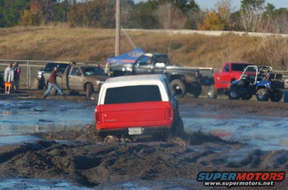 1978 Ford Bronco rear view stuck in mud pit with other vehicles nearby