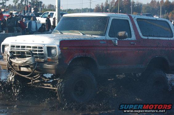 Muddy two-tone red and white Ford Bronco with winch on front bumper going through mud pit