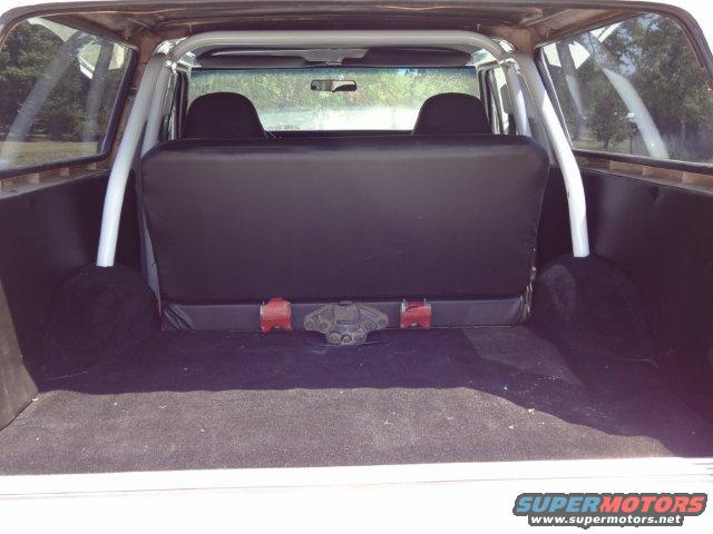 Interior of a white SUV, showing black rear seats, roll cage, and carpeted cargo area