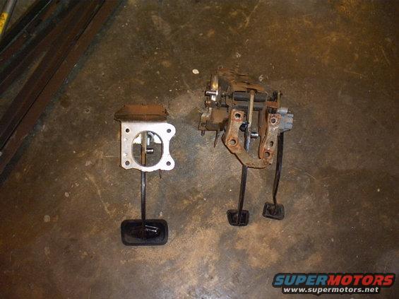 Two sets of car pedals, one with a single pedal and the other with two pedals, on a concrete floor