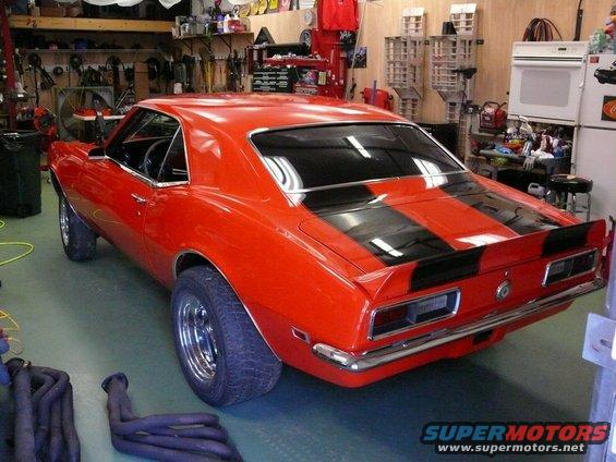 Red 1968 Chevrolet Camaro with black racing stripes, chrome trim, and aftermarket wheels, viewed from the rear three-quarter angle