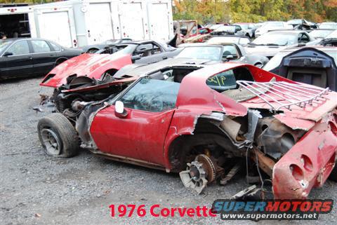 Wrecked red 1976 Chevrolet Corvette in a junkyard with other cars