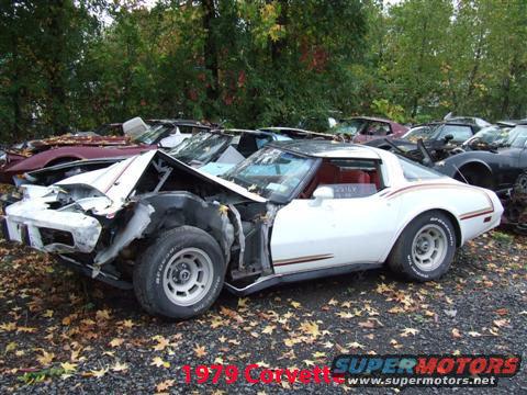 Damaged white Corvette with front end smashed, parked in a junkyard with other cars