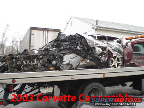Wrecked red 2003 Chevrolet Corvette on a flatbed tow truck, heavily damaged front end