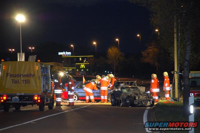 Wrecked black sports car and blue sedan with emergency responders at night
