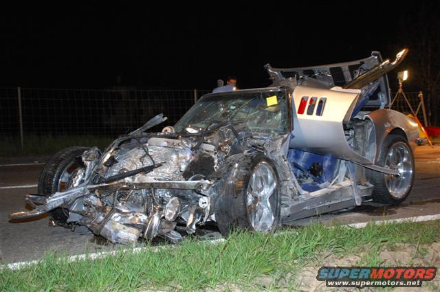 Heavily damaged silver sports car, front end destroyed, driver's side door open