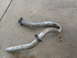 1984 Ford Bronco - Two bent exhaust pipes lie on a concrete surface, showing signs of wear and rust.