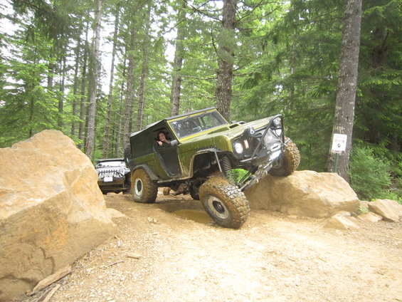 Green 1974 Ford Bronco climbing rocks on a trail, with another SUV behind it