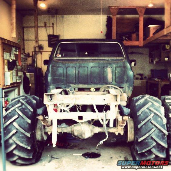 Rear view of a monster truck with massive tires, stripped down chassis, in a garage