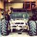 1983 Chevrolet C/K Pickup - Monster truck with oversized tires and a stripped-down rear chassis sits in a garage, awaiting further modifications.
