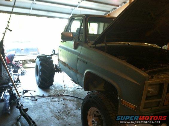 Green 1983 Chevrolet C/K Pickup truck with hood open and large tires in garage