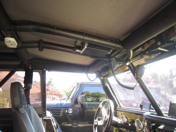 Interior of a Jeep with roll cage, CB radio mounted overhead, and another Jeep visible outside