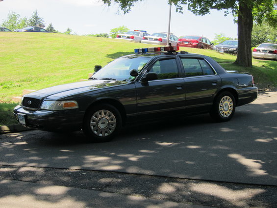 Dark sedan police car with light bar, 3/4 front view. Likely 2003-2011 model