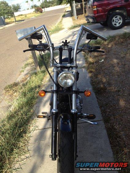 Motorcycle front view with tall handlebars and chrome accents parked on a sidewalk