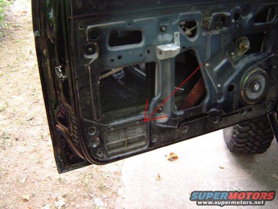 Car door interior with visible speaker and window mechanism, showing rust and dirt