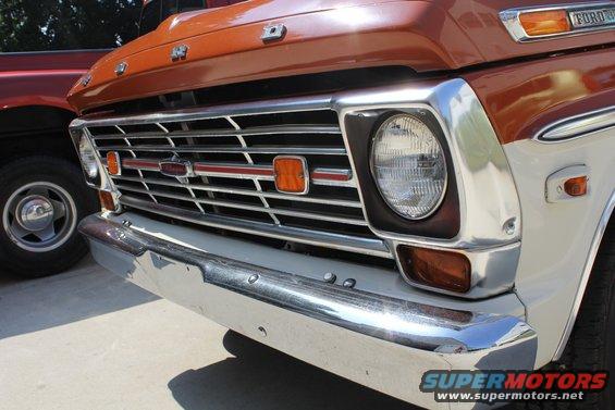 Orange and white Ford F-Series truck front grille and bumper, chrome accents, orange turn signals, another red truck visible to the left