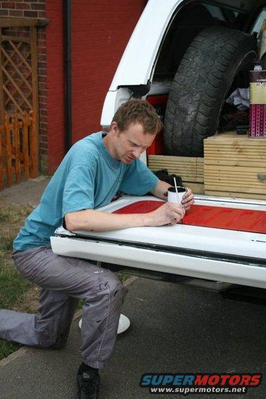 Man painting red stripe on white tailgate of a vehicle with spare tire inside