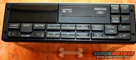 Car stereo with Ford logo, cassette deck, and numerous buttons including POWER, AUDIO, AM/FM, VOLUME, CLOCK, SCAN, TUNE, REW, FF, PLAY, PROG, and EJECT