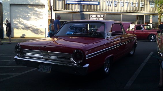 1964 Ford Fairlane coupe parked in front of a Westlife auto shop, with a red pickup truck in the background