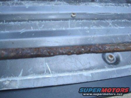 Rusted metal bar on gray textured surface with visible scratches and two circular fasteners