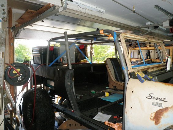 1961 International Scout 800 interior with roll cage installed, in a garage. Door has 'Scout All Wheel' badging