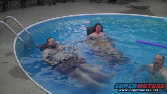 Three men relax in an above-ground swimming pool, with a purple pool noodle visible