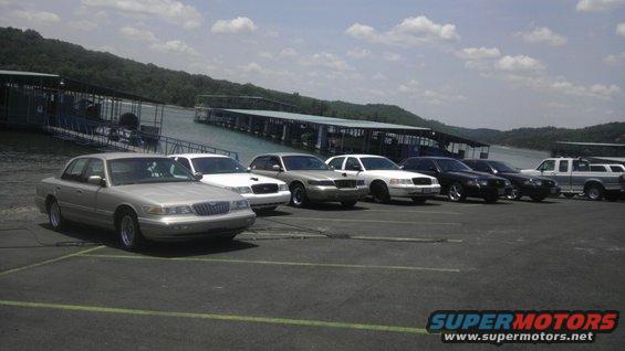 Several sedans and trucks parked near a lake with docks