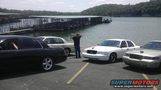 Four sedans parked by a lake with docks in the background. One person is standing between two cars