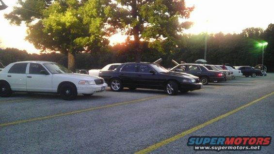 Several sedans parked in a lot at dusk, including a white Crown Victoria and a black Mercury Grand Marquis