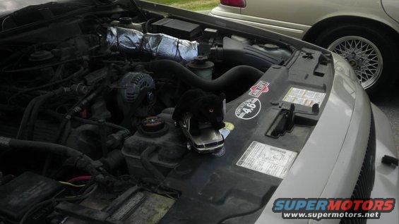 engine bay of a car with a toy car and a black panther figure on the hood. Another car is visible in the background