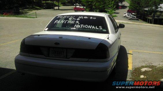 Rear view of a white sedan with 'Follow me to the Panther NATIONALS' written on the back window. License plate is visible