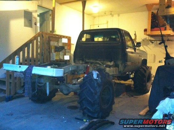 Black pickup truck chassis with large tires, undergoing modifications