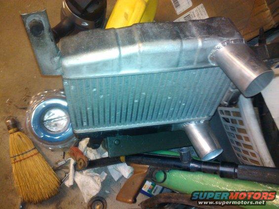 Aluminum radiator with silver inlet and outlet pipes, next to a broom and a toy gun
