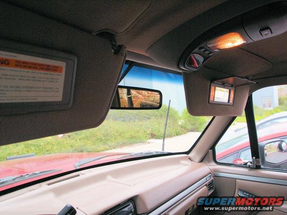 Interior view from driver's side, showing sun visors, rearview mirror reflection, and dashboard. Another red vehicle is visible outside