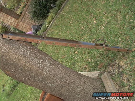 Rusted metal bracket with holes, lying on grass next to a tree trunk
