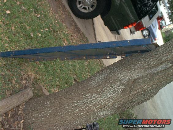 Blue metal panel leaning against a tree trunk. Part of a dark SUV and a blue car are visible in the background