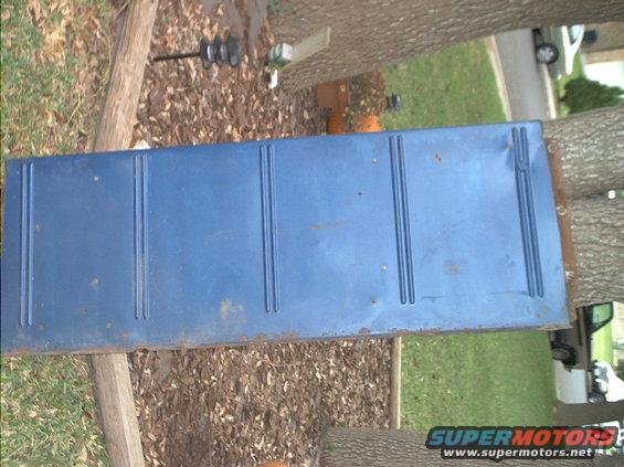 Blue tailgate with vertical ridges, resting on wood and ground