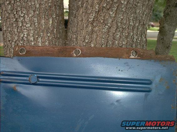 Blue metal panel with two horizontal ridges and a circular indentation, attached to a wooden strip with visible screw holes