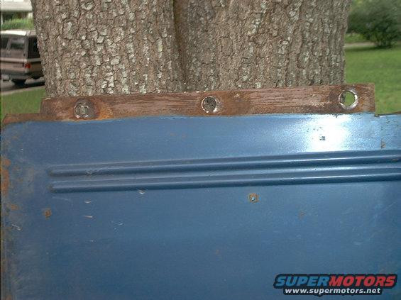 Close-up of a blue metal panel with two horizontal ridges and rust along the top edge
