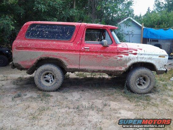 Mud-covered red and white Ford Bronco with flame decals on the front fender