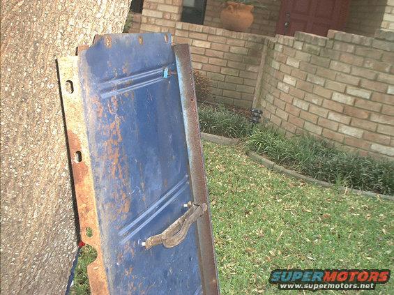 Blue tailgate with chrome handle leaning against tree