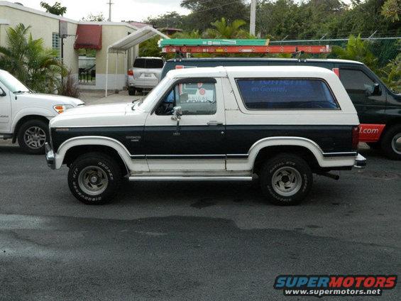 Two-tone Ford Bronco parked next to a white SUV and a dark pickup truck with ladders on top