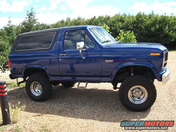 Blue Ford Bronco with lifted suspension and aftermarket wheels parked on gravel