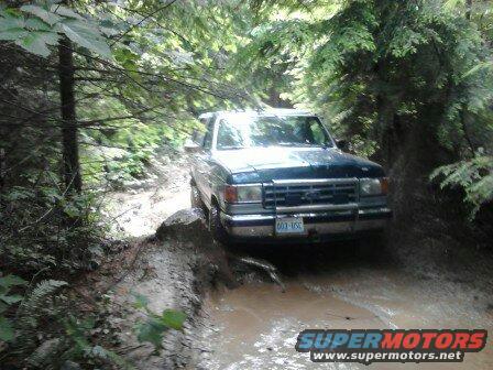 Dark blue 1987 Ford Bronco navigating a muddy trail in a forest